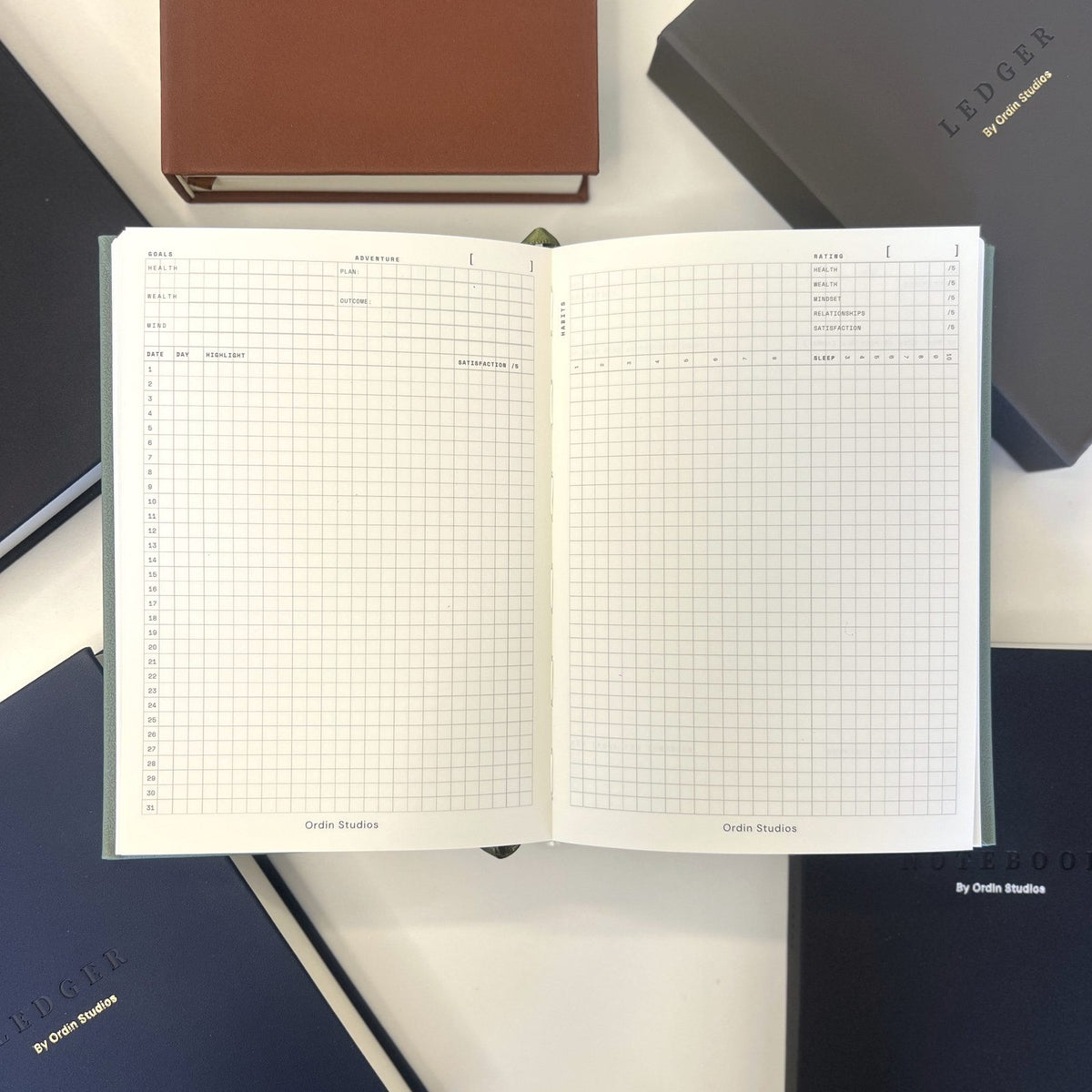 The Ledger open to its monthly dashboard spread, surrounded by its leather covers on a white desk